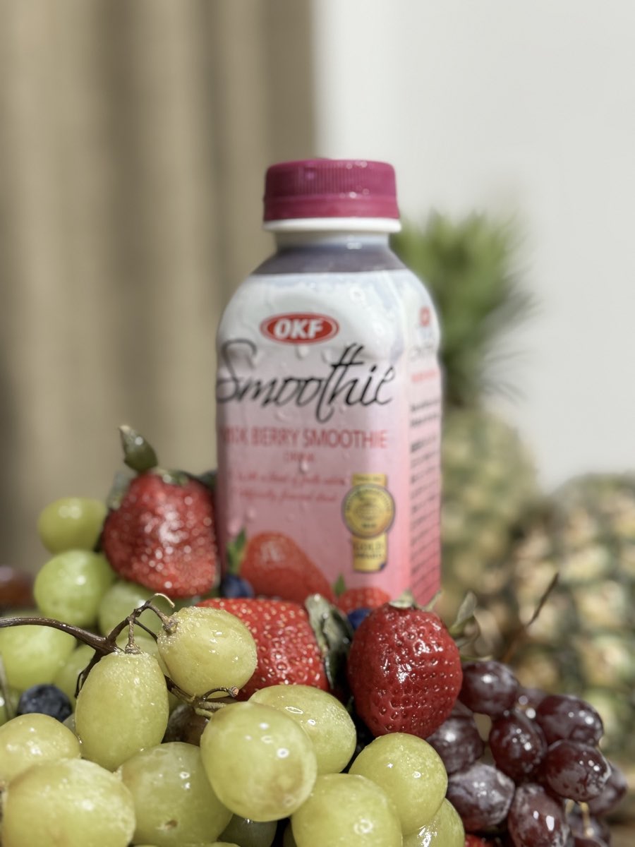 Upright yellow and mixed berry OKF Korean smoothie bottles surrounded by fresh fruit